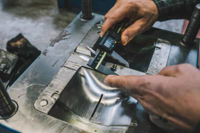 Hands measuring metal mold with caliper