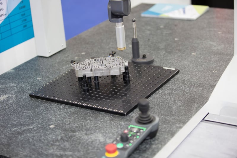 Joystick-controlled CMM inspecting metal part.