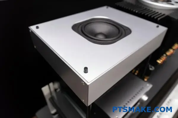 Rectangular aluminum speaker housing next to audio system components